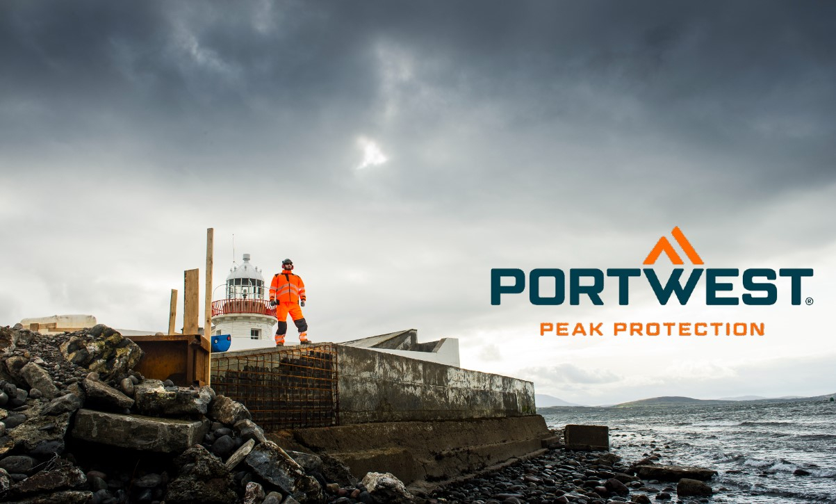 Um trabalhador que veste roupas laranja de alta visibilidade está num estaleiro de construção rochoso junto a um farol, com o logótipo da Portwest e o slogan 'Pick Protection' na foto. Existe um link que leva às nossas roupas de trabalho multi-normas.