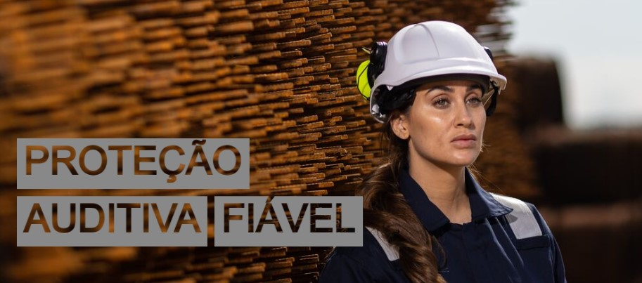 Imagem de uma trabalhadora com um fato de trabalho azul escuro, capacete branco e proteção auditiva PS47 amarela em frente a uma parede feita de ferro reforçado.