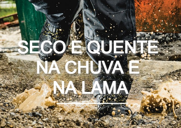 Trabalhador com calças de chuva e botas a entrar numa poça. A lama está a espirrar e pode ver um estaleiro de obras ao fundo. Existe um link para os nossos sapatos impermeáveis.